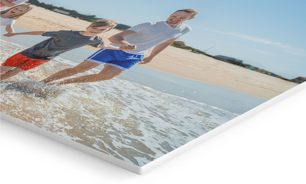 Lienzo fotográfico personalizado que muestra a un padre y dos niños corriendo y jugando en la orilla de la playa, con el mar y la arena.